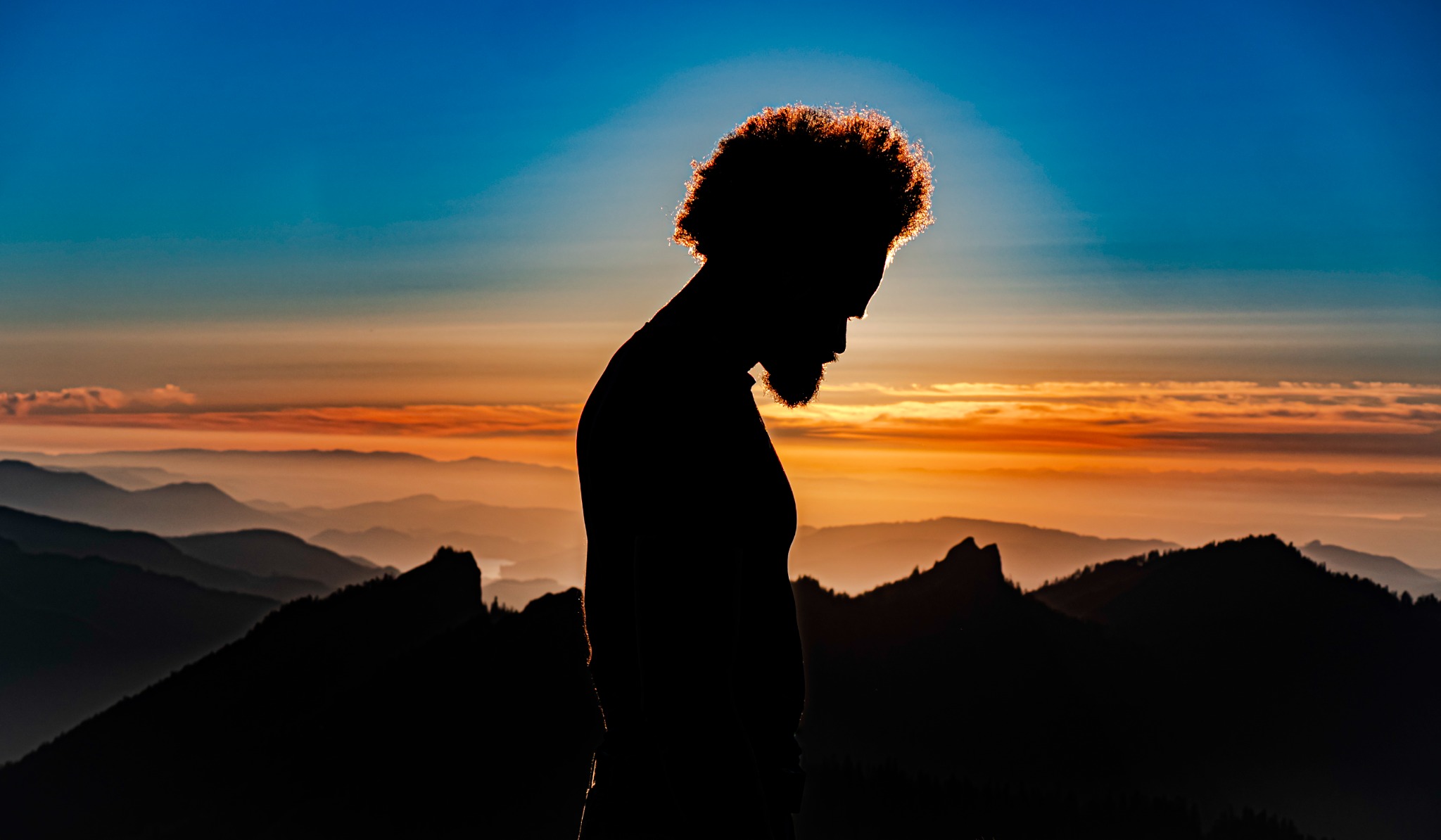 A silhouetted figure against a golden sky and layers of mountain ridges